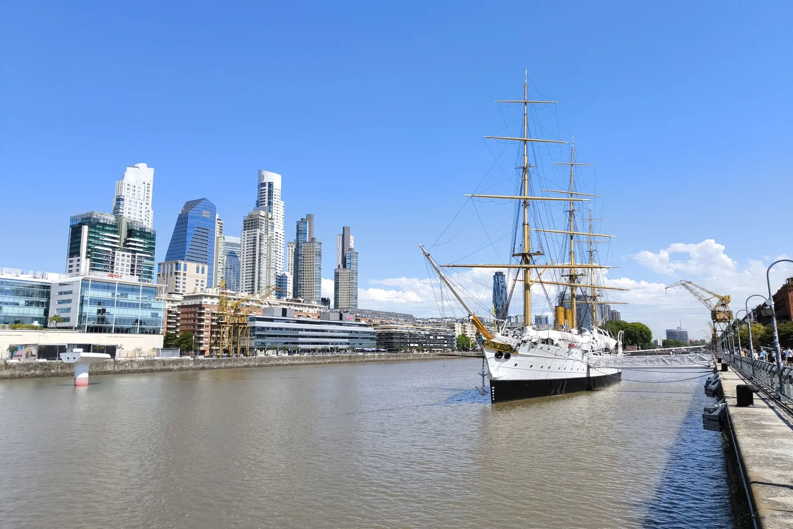 Puerto Madero con la Fragata Sarmiento amarrada y los edificios de fondo, un día de cielo azul.