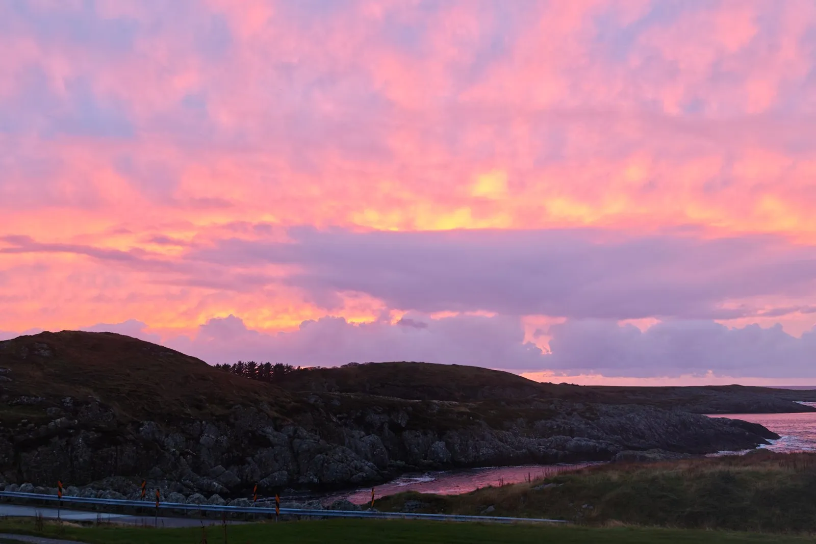 Cielo rosa y violeta sobre un fiordo, con una loma oscura y el agua quieta.